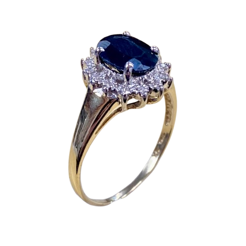 Ladies 9ct Yellow Gold 15 Stone Diamond & Sapphire Ring. Oval Sapphire In Rhodium 4 Claw Setting, Surrounded by 14 Single Cut Diamonds Illusion Bead Set in Rhodium Plated Basket, In Swept Up Shoulders. TDW 0.07ct. Size M/6.5, With Valuation Certificate – (NG 1307520)